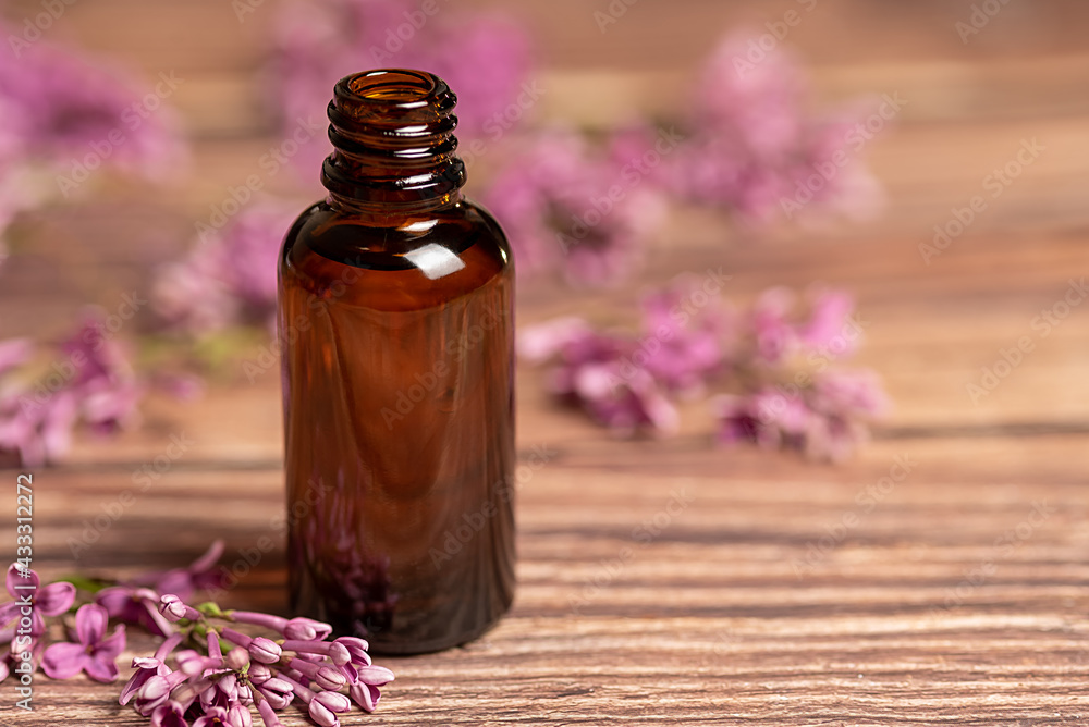 Cosmetic oil stands on a wooden background. Purple flowers lie on the table. Cosmetic oil stands on a wooden background. Purple flowers lie on the table.
