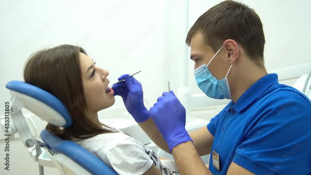 Slow Motion portrait of young dentist in mask examining teeth of female client i Slow Motion portrait of young dentist in mask examining teeth of female client i