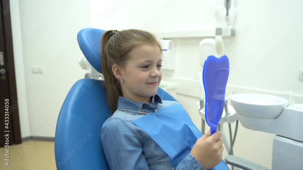 Positive little girl holding a mirror, sitting in a dental chair.