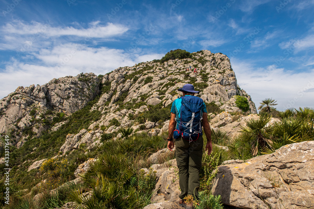 Fototapeta premium Hiker equipped with a backpack, walking through a rugged and stony mountain, on a morning with cloudy skies, in Sierra de Segaria, Alicante (Spain).