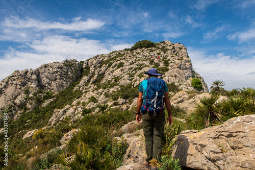 Hiker equipped with a backpack, walking through a rugged and stony mountain, on a morning with cloudy skies, in Sierra de Segaria, Alicante (Spain).