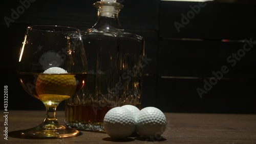 BOURBON CUP WITH GOLF BALLS ON WOODEN TABLE WITH TENUE LIGHTING AND CREATIVE MOVEMENT