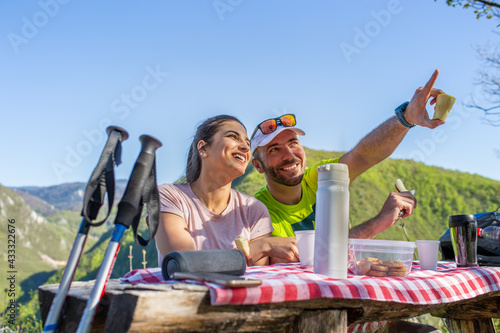 A couple on the hiking tour is having a picnic at the top of the mountain.