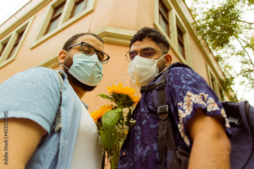 Retrato frontal contrapicado de pareja de novios gay usando mascarillas en la calle  photo