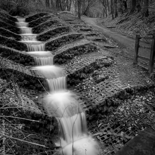 A black and white photograph of a manmade waterfall in Haigh Woodlands Park, Haigh Plantations, Wigan, Greater Manchester. photo