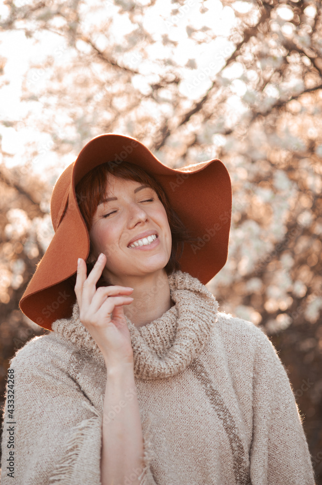 Young smiling girl in a hat on a background of flowering trees Young smiling girl in a hat on a background of flowering trees
