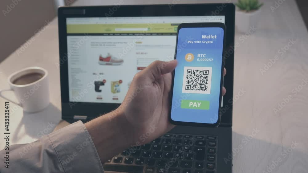 POV shot of a man sitting at the desk, holding a smartphone in the left hand, bringing it closer to a laptop screen, scanning QR code and paying with crypto wallet mobile app POV shot of a man sitting at the desk, holding a smartphone in the left hand, bringing it closer to a laptop screen, scanning QR code and paying with crypto wallet mobile app
