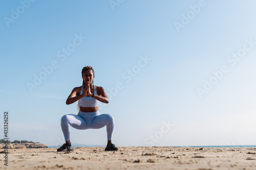 African young woman doing exercises and stretching outdoors with beach on background in summer vacation - Focus on face