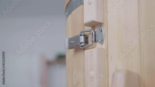 Closeup of door of cedar phytobarrel. Hand of master uses metal lock on latches