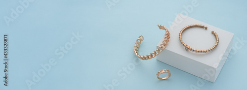 Panoramic shot of golden bracelets and ring on white box on blue background