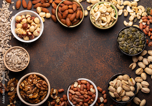 Selection of assorted raw nuts and various seeds in bowls on brown stone background from above, healthy source of energy, fat and vegetarian protein, space for text