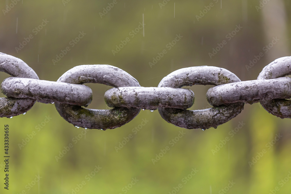 Thick iron chain with water drops on links in the rain on blurred background Thick iron chain with water drops on links in the rain on blurred background