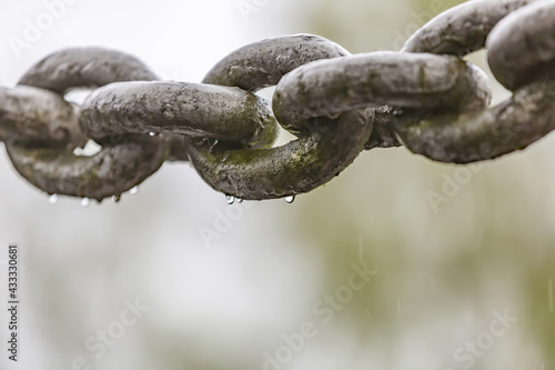 Thick iron chain with water drops on links in the rain on blurred background