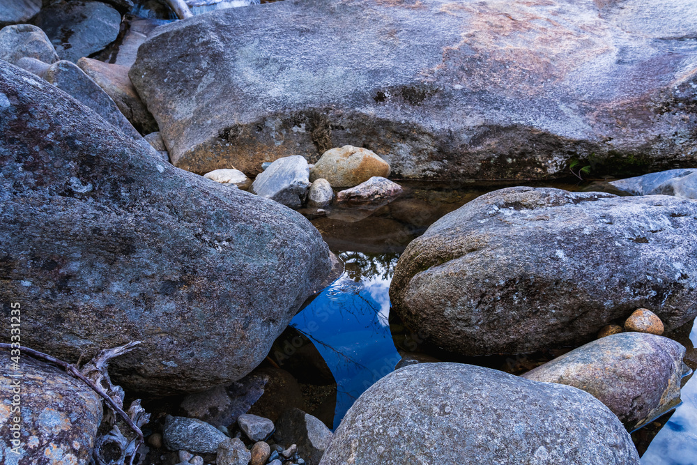 Obraz premium Reflection of the sky on the surface of the crystal clear Pemigewasset River among huge smooth stones in spring. Franconia Falls by the Lincoln Forest Trail in the White Mountains National Forest, NH