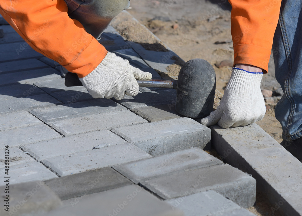 A worker knocks on paving slabs, levels a concrete block with a construction hammer, close-up. A worker knocks on paving slabs, levels a concrete block with a construction hammer, close-up.