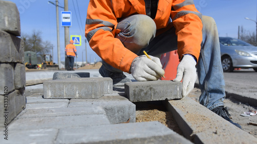 A worker makes a marking with a pencil on a concrete block, paving slabs are laid out on the ground, road works are carried out.