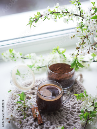 Spring still life on the windowsill, a cup of espresso coffee, ground coffee in a jar. Blooming branches of white cherry