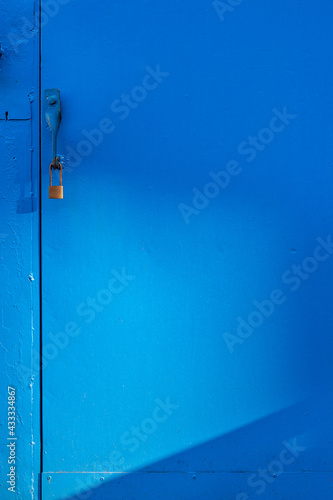 工場の青色の鉄製扉にかかる金色の南京錠、太陽の陽の光の作る淡い影 © captainT