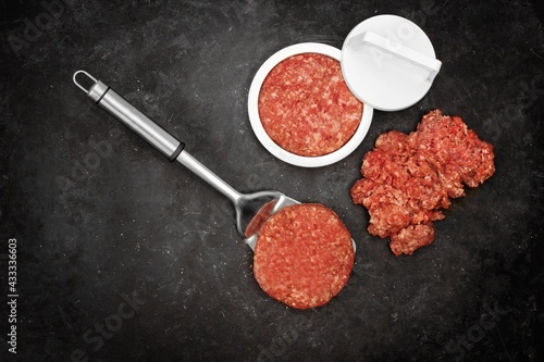 Patty Press and Raw Burgers on Wooden Board. Plastic Burger Stuffer with Grill Tools, Top View. Beef and Pork Mince Patties on Rustic Black Background, Overhead View.