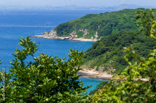 Beautiful summer landscape with an island. The winding steep rocky shores of the island are covered with green bushes against the backdrop of the blue sea.