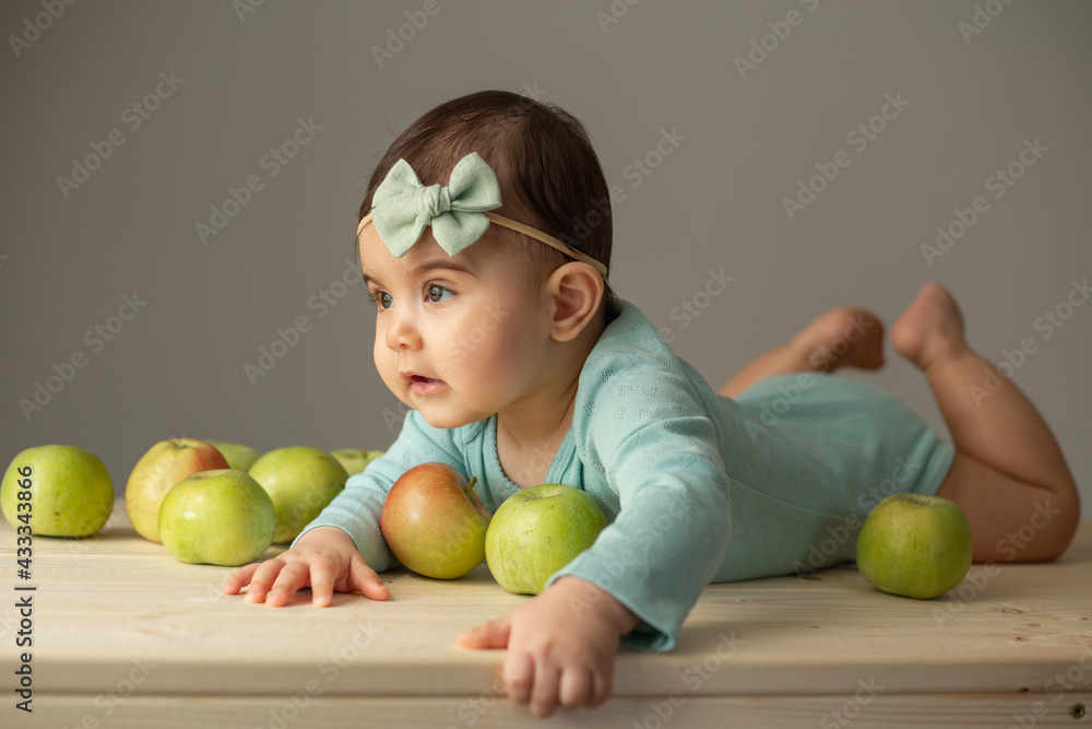 portrait of a little girl in a green bodysuit on a wooden table with fresh green apples. Natural products for children. High quality photo portrait of a little girl in a green bodysuit on a wooden table with fresh green apples. Natural products for children. High quality photo