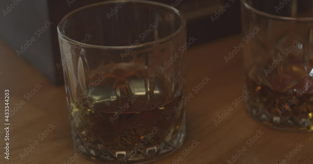 Dropping stainless steel whiskey ice cubes in a crystal whisky tumbler. Dropping stainless steel whiskey ice cubes in a crystal whisky tumbler.