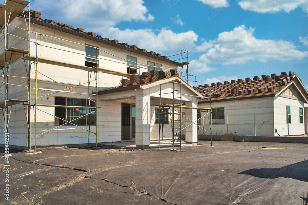 Concrete roofing tile installation with roof tiles lined up in rows on a residential modern home build with a patio cover and scaffolds and backyard preparation Concrete roofing tile installation with roof tiles lined up in rows on a residential modern home build with a patio cover and scaffolds and backyard preparation