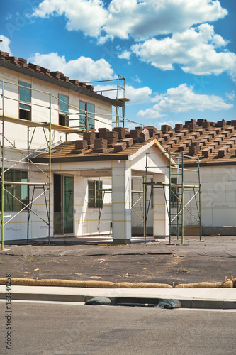 Concrete roofing tile installation with roof tiles lined up in rows on a residential modern home build with a patio cover and scaffolds on a sunny day with beautiful blue skies
