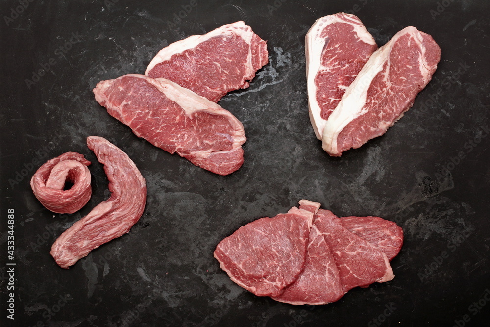 Various Raw Steaks. Sirloin Beef Steaks, Overhead View. Many Raw Striploin Steaks from Marbled Beef on Black Background. Group of Black Angus Beefsteaks. Raw Sirloin Cuts. Uncooked Prime Beef Steaks.