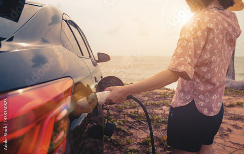 EV car charging power hybrid electric car at the charging station, hand holding charger inserting the pump, environmentally friendly lifestyle transportation vehicle traveling vacation evening sunset