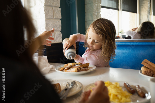 Mother with toddler daughter pouring ketchup in diner photo