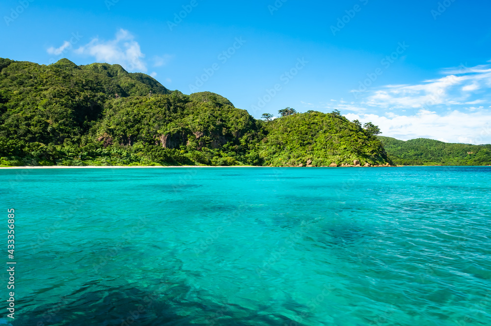 Impressive turquoise sea with an uneven surface due to the gentle wind, green mountains, blue sky, white clouds. This stunning scene of a natural environment seen from a boat.