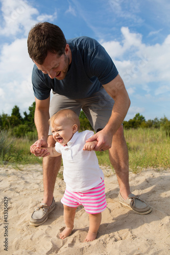 Mid adult man holding baby daughters hands while toddling in sand photo