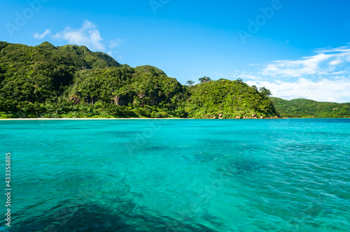 Impressive turquoise sea with an uneven surface due to the gentle wind  green mountains  blue sky  white clouds. This stunning scene of a natural environment seen from a boat.