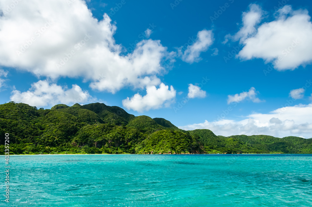 Impressive turquoise sea looking like a pool with an uneven surface due to the gentle wind, green mountains, blue sky, white clouds. This stunning scene of a natural environment seen from a boat.