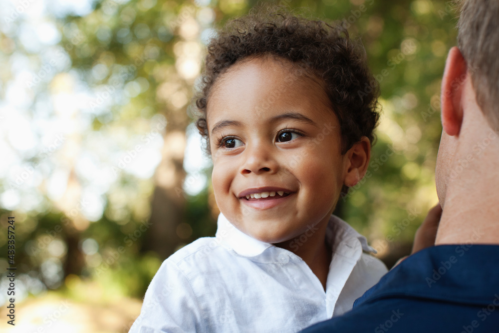 Over shoulder view of father carrying preschool boy looking away smiling Over shoulder view of father carrying preschool boy looking away smiling
