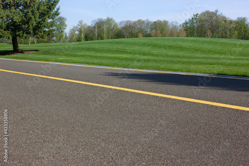 Asphalt road for cyclists and pedestrians through the green lawn in the park. A walk in the spring park.
