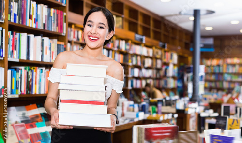 Smiling cheerful positive attractive girl holding pile of books bought in bookstore
