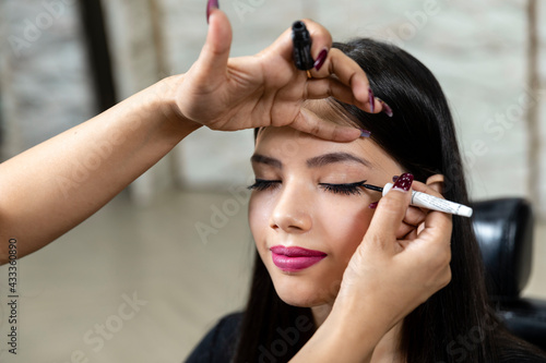 A young Indian model at a beauty salon, makeup artist applying eyeliner on customer, makeup and beauty parlour concept.