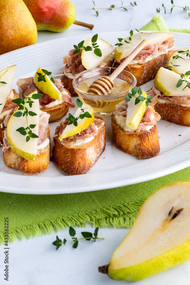 A platter of pear and prosciutto appetizers topped with thyme, and a half pear in front. A platter of pear and prosciutto appetizers topped with thyme, and a half pear in front.