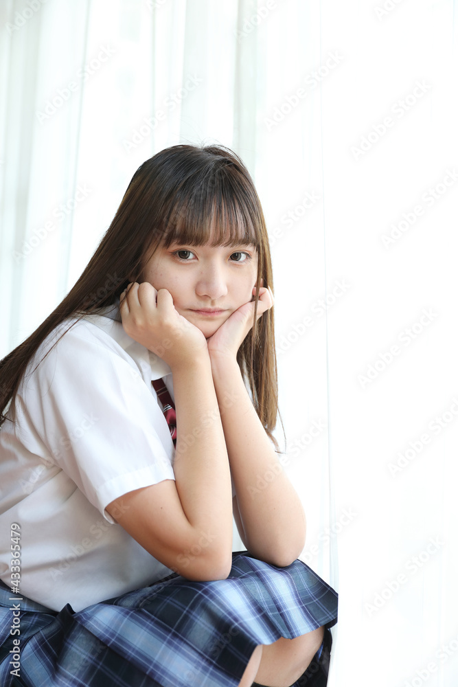 Portrait japanese school girl uniform sitting and look at camera in white tone bed room Portrait japanese school girl uniform sitting and look at camera in white tone bed room