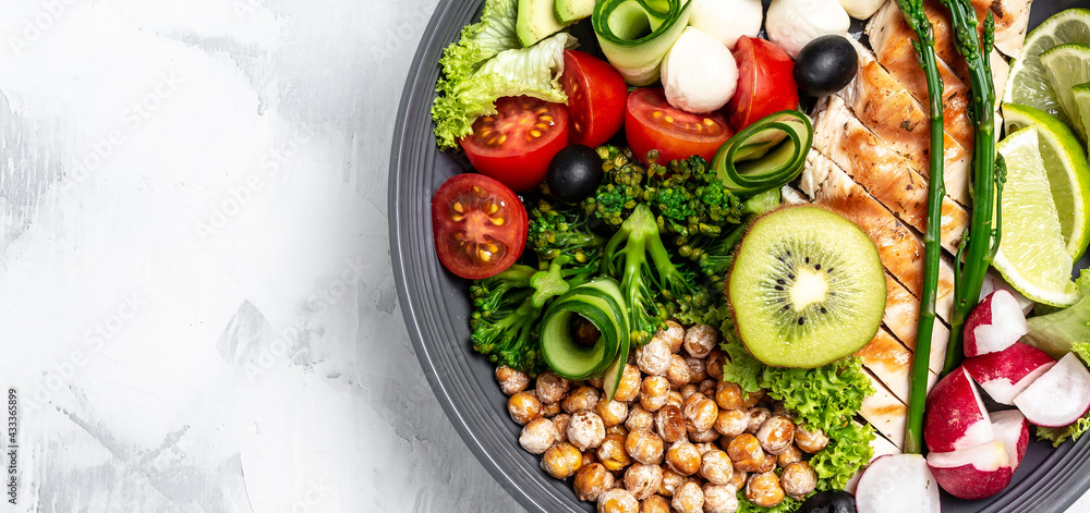 Buddha bowl with kale salad, avocado, asparagus, chickpeas, broccoli, radish, chicken, cucumber, tomatoes, olives and mozzarella. Long banner format, top view