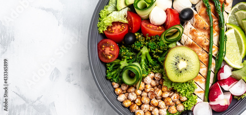 Buddha bowl with kale salad, avocado, asparagus, chickpeas, broccoli, radish, chicken, cucumber, tomatoes, olives and mozzarella. Long banner format, top view