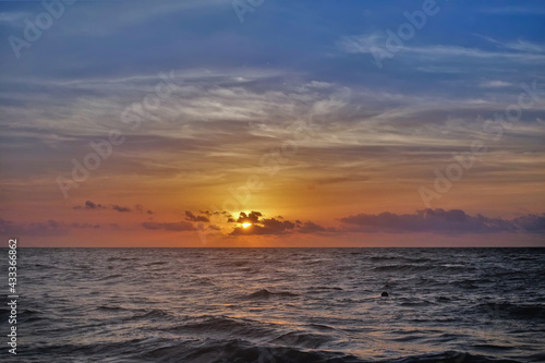 Dawn over the Caribbean Sea. The sun shines through the gap in the clouds. The blue sky is backlit with orange. Small waves on the water. Mexico © Вера 