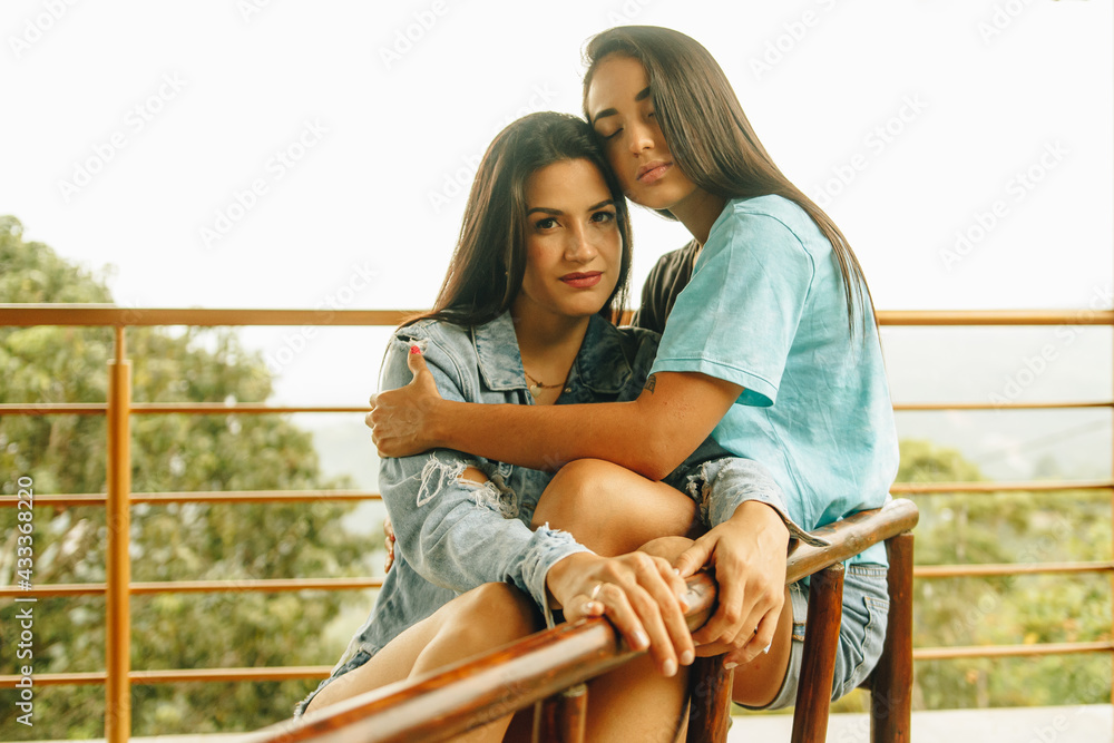 Joven lesbiana sentada sobre las piernas de su novia en una banca Joven lesbiana sentada sobre las piernas de su novia en una banca