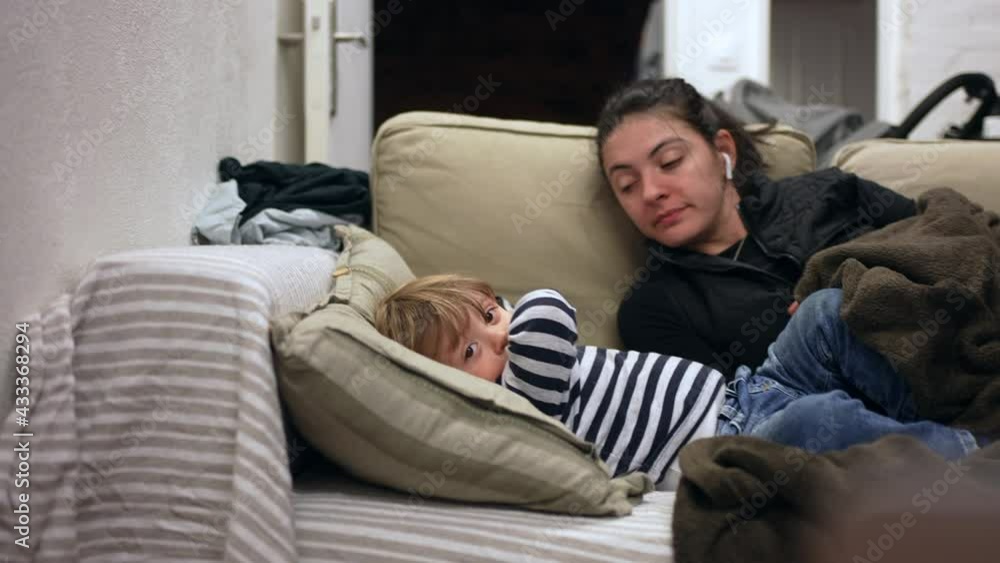 Sleepy mother lying down in sofa with baby toddler, candid and real life Sleepy mother lying down in sofa with baby toddler, candid and real life