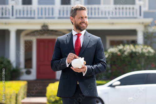 Businessman putting money in piggy bank on home background. Handsome caucasian man holding piggybank for money for savings.