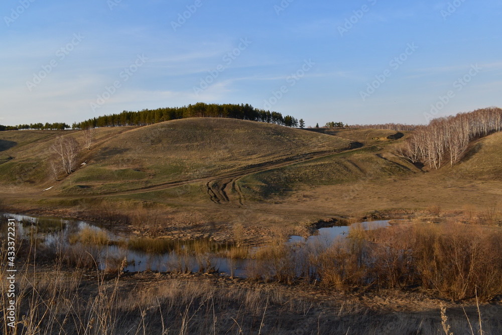 Beautiful landscape in early spring. View of hilly terrain, trees, country road and stream.