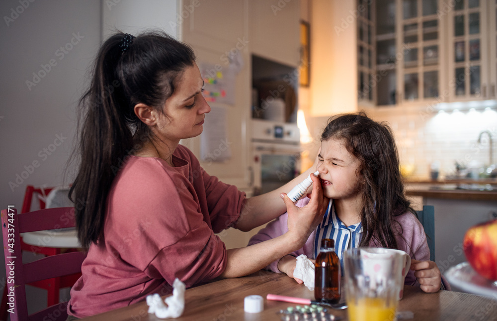 Mother looking after sick small daughter at home, using nasal spray. Mother looking after sick small daughter at home, using nasal spray.