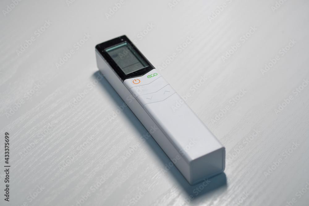 Air conditioner remote control on white table in front of bed Air conditioner remote control on white table in front of bed